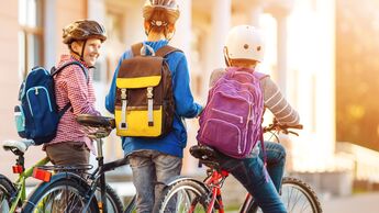 Children with rucksacks riding on bikes in the park near school
