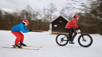 Fahrradfahren im Winter Skifahrer im Schlepptau