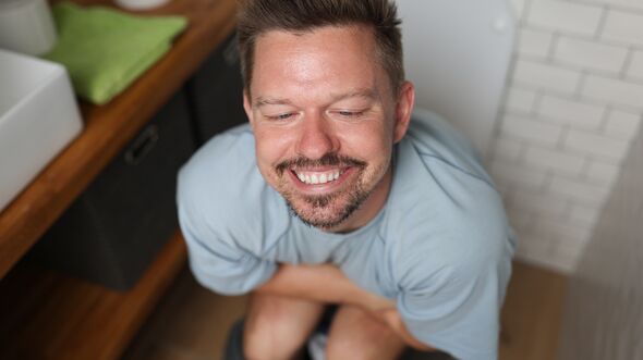 Man with satisfied smile sits on toilet