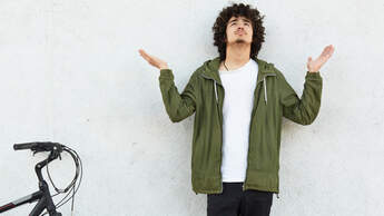 Oh God, help me please! Plesding male teenager spreads palms and raises head, prays for something while stands against white background near bike. People, body language and lifestyle concept