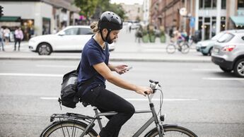 Side view of man using mobile phone while riding bicycle on city street