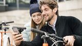 Smiling couple with bicycles and cell phone in the city
