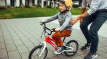 Vater schiebt Kind auf kleinem Fahrrad