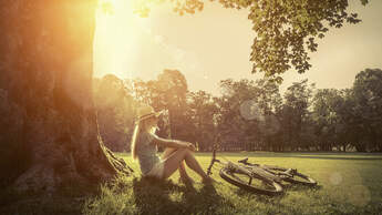 Woman sitting under sun near her bicycle in the park