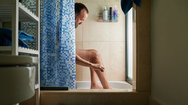 portrait of an intimate moment of a middle-aged man with beard shaving his leg in the bathroom at home